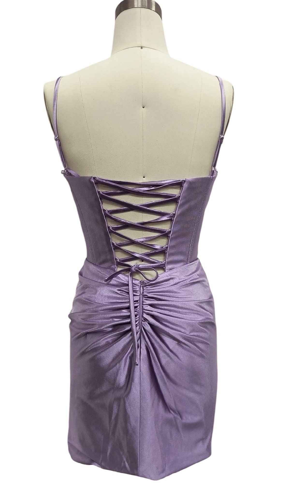 Back view of Short Lilac Corset Hoco Dress: 12623 on a mannequin, featuring shiny lilac fabric, spaghetti straps, lace-up corset back, and ruched detailing at the lower back.